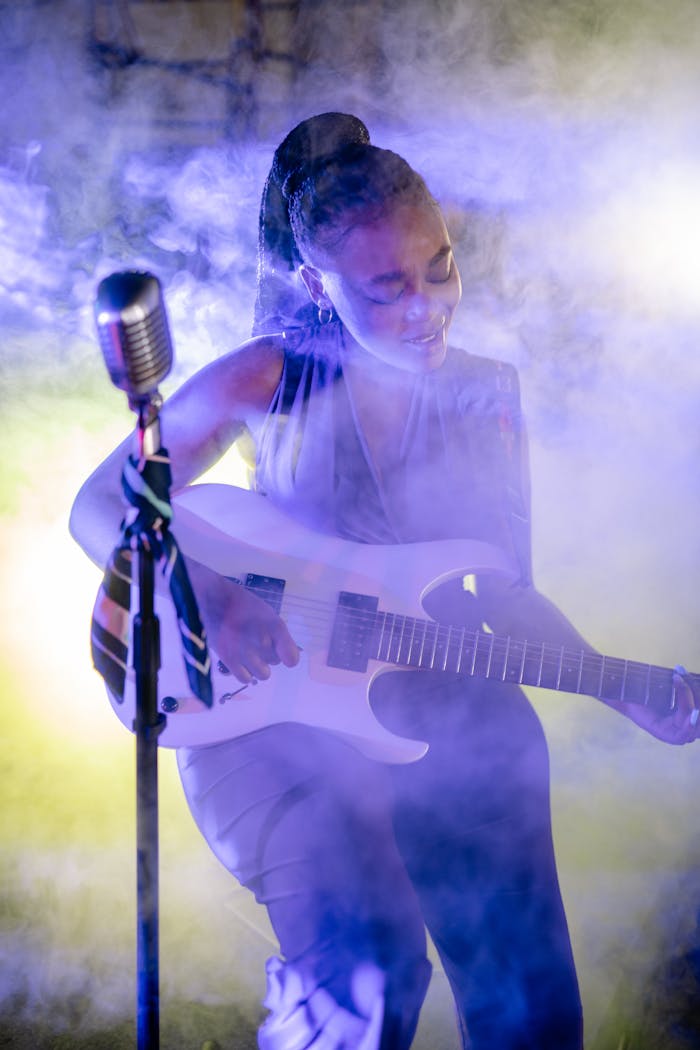A vibrant live performance featuring a skilled female guitarist amid colorful stage lighting and smoke.